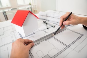 Close-up Of Engineer Drawing Diagrams In Front Of House Model On Blueprint
